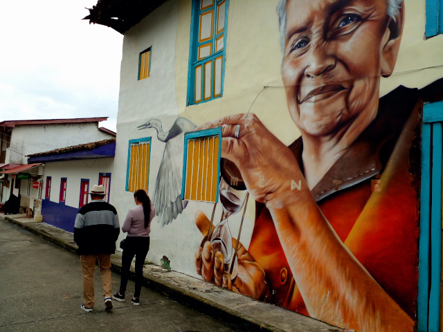 People walking along a street in Pijao beside an artistic mural.